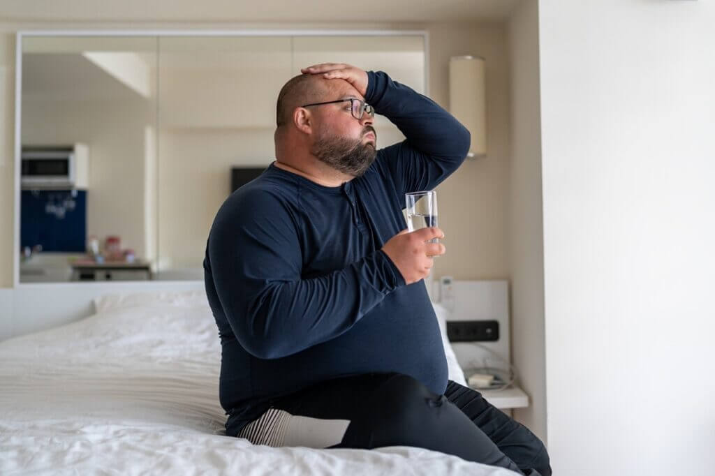 Person experiencing allergy symptoms holding water glass indoors